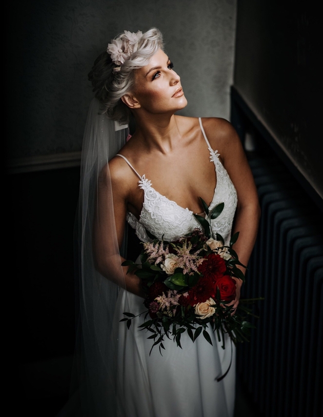 Bride looks up clutching bouquet whilst illuminated in a darkened space