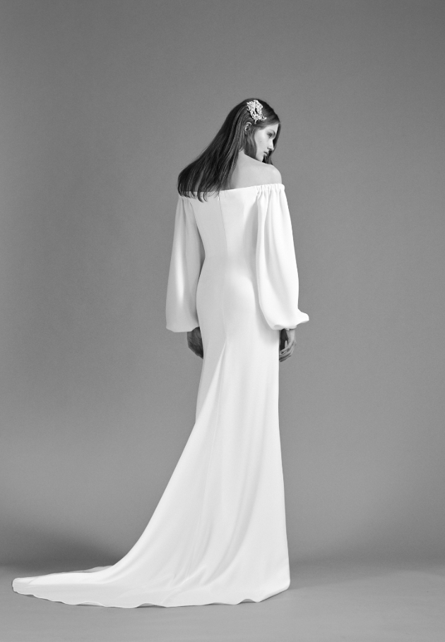 Black and white image of a model wearing a wedding dress with long cuffed sleeves and a headpiece