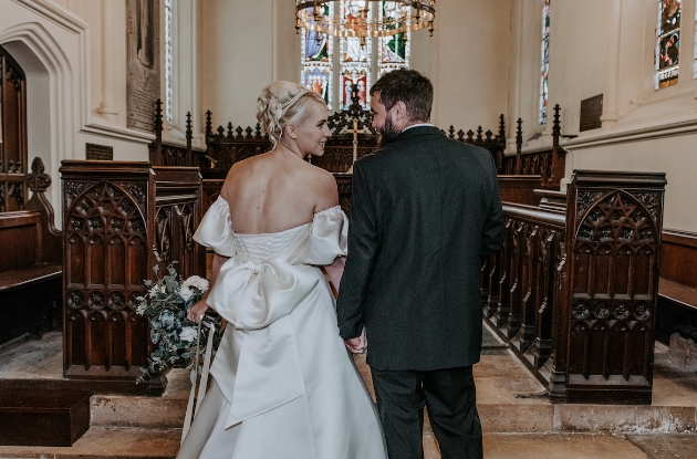 bride in low back dress walking down aisle in church with groom