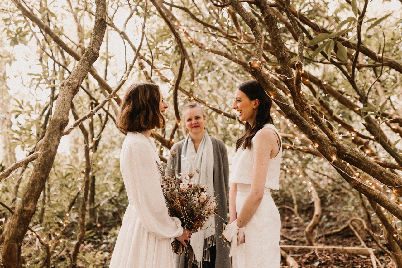 couple in wedding dresses tying the knot outside in the woods with a celebrant