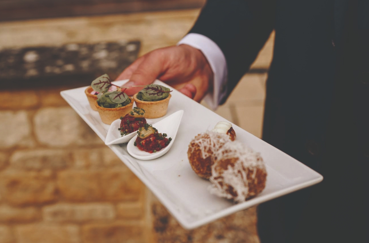 three varieties of canapé on a serving plate held by formal waiter