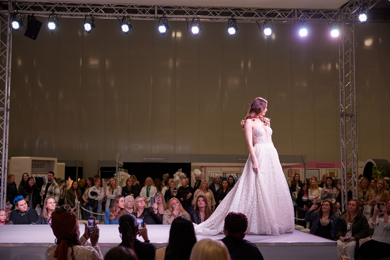 model in wedding dress walking on stage at fashion show